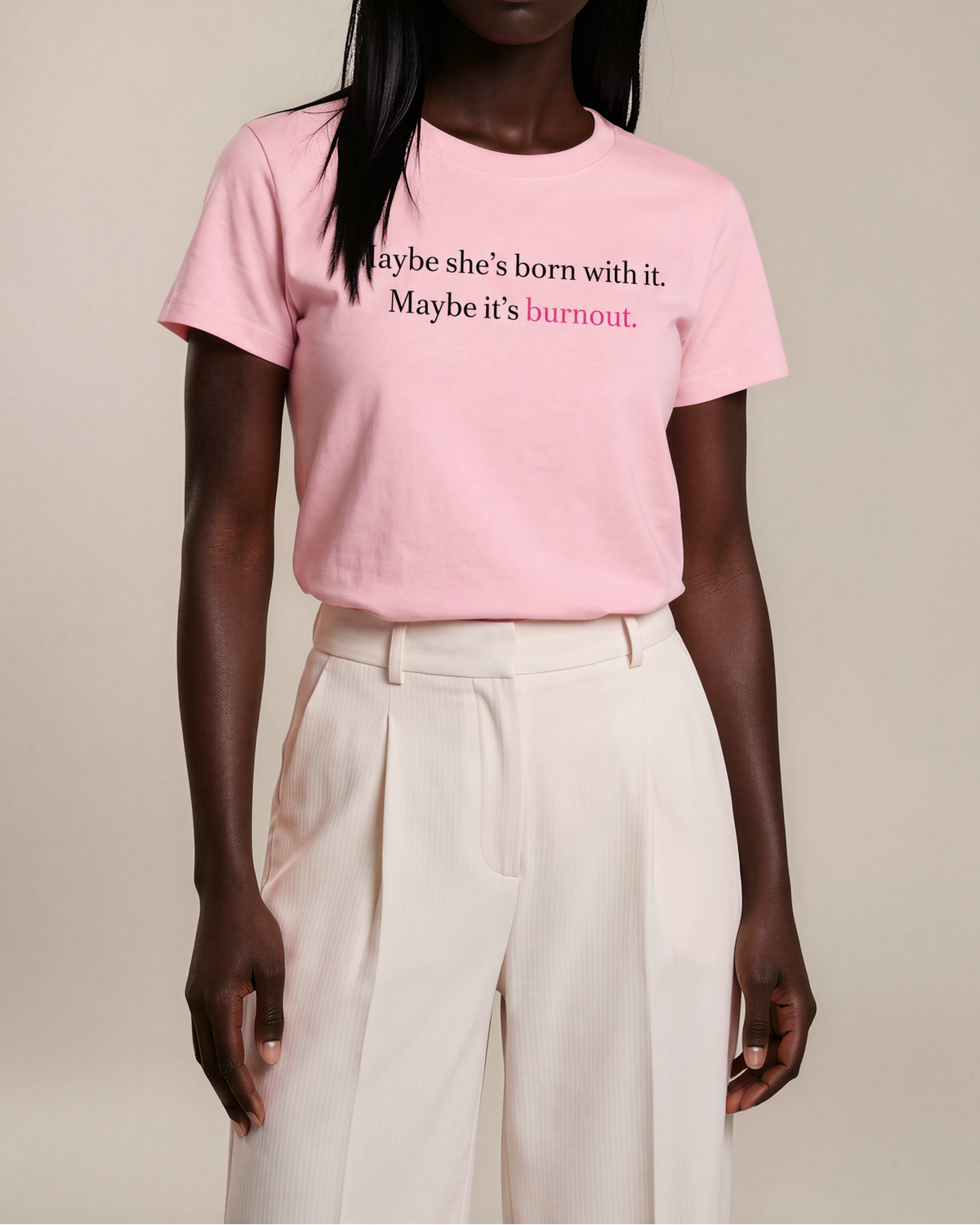 Model wearing a pink Burnout women’s slim-fit tee reading ‘Maybe she’s born with it. Maybe it’s burnout.’ with light trousers